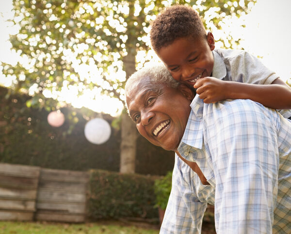Young black boy climbing on his grandfatherâs back in garden Young black boy climbing on his grandfatherâs back in garden
